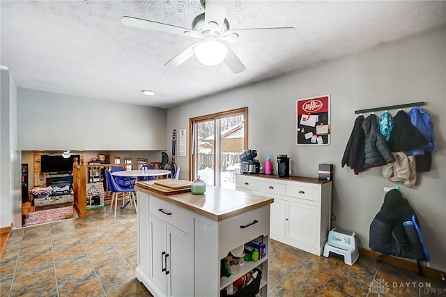 kitchen featuring a center island, ceiling fan, a textured ceiling, a fireplace, and white cabinetry