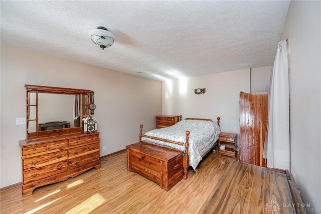 bedroom with a textured ceiling, light wood finished floors, and baseboards