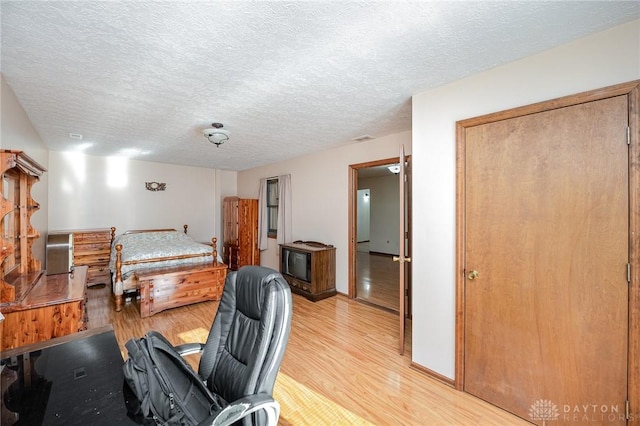 bedroom with a textured ceiling, light wood finished floors, visible vents, and baseboards