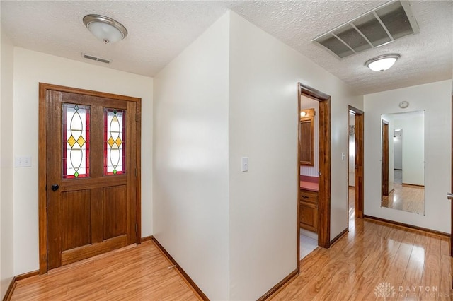 entrance foyer with light wood-style floors, visible vents, and a textured ceiling