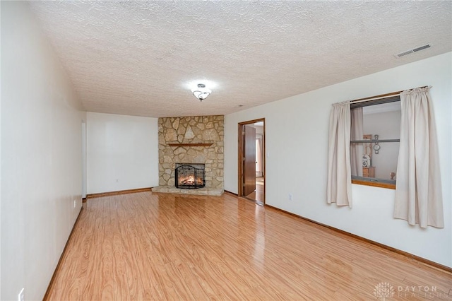 unfurnished living room featuring light wood-style floors, visible vents, a stone fireplace, and a textured ceiling