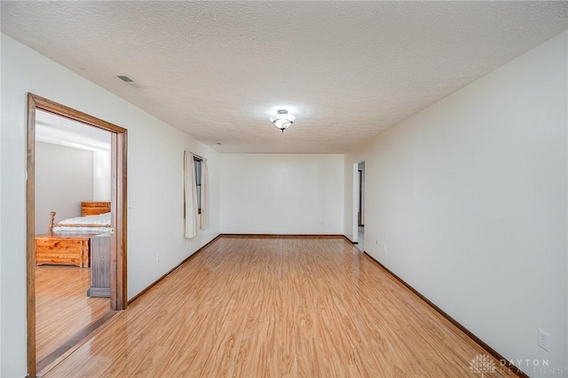 unfurnished room featuring visible vents, a textured ceiling, baseboards, and wood finished floors