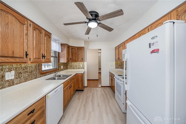 kitchen featuring brown cabinets, white appliances, light countertops, and a sink