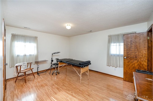 game room featuring a textured ceiling, a healthy amount of sunlight, visible vents, and light wood-style floors