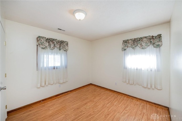 empty room with wood finished floors, visible vents, and baseboards