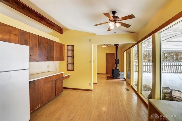 kitchen featuring ceiling fan, white refrigerator, vaulted ceiling with beams, light hardwood / wood-style floors, and a wood stove