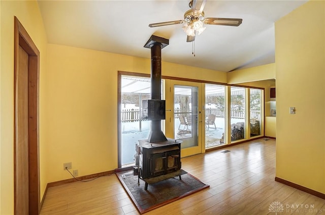 doorway to outside with light hardwood / wood-style floors, a wood stove, ceiling fan, and lofted ceiling