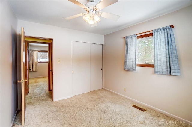 unfurnished bedroom featuring ceiling fan, light colored carpet, multiple windows, and a closet