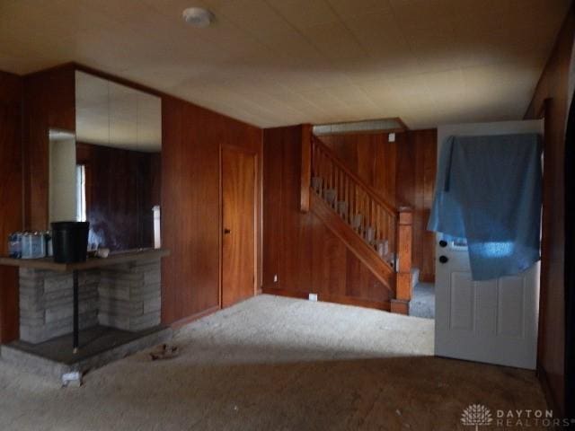 living area featuring stairs, carpet flooring, and wood walls