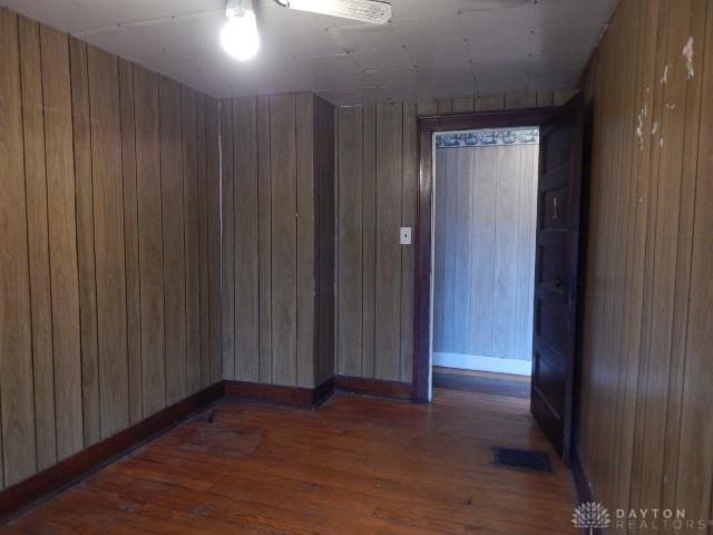 unfurnished room featuring visible vents, wood walls, baseboards, and wood finished floors