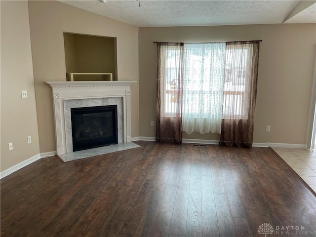 unfurnished living room featuring a fireplace, wood-type flooring, a textured ceiling, and plenty of natural light