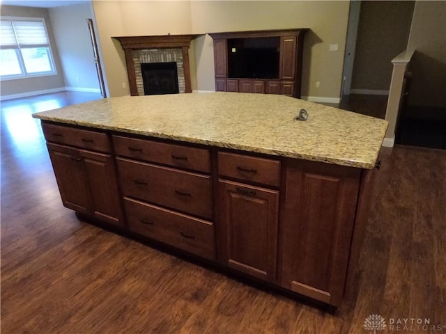 kitchen featuring dark brown cabinets, dark hardwood / wood-style flooring, a brick fireplace, and a kitchen island