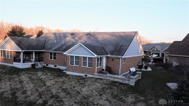 back house at dusk featuring a lawn