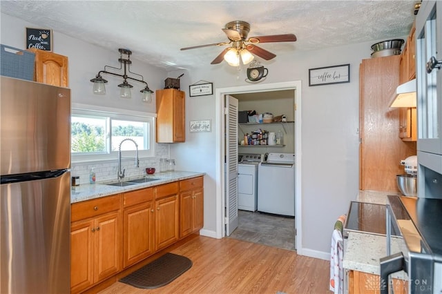 kitchen with backsplash, light wood-type flooring, freestanding refrigerator, independent washer and dryer, and a sink