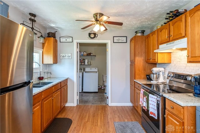 kitchen featuring washer / dryer, a sink, appliances with stainless steel finishes, under cabinet range hood, and backsplash