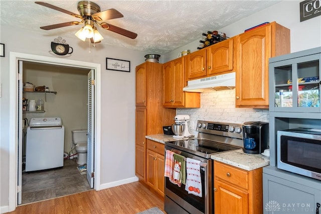 kitchen featuring under cabinet range hood, light wood-type flooring, decorative backsplash, washer / dryer, and stainless steel appliances