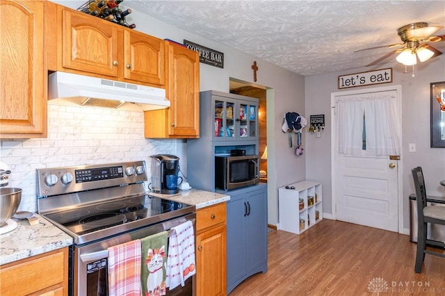 kitchen featuring light wood-style flooring, under cabinet range hood, tasteful backsplash, a textured ceiling, and appliances with stainless steel finishes