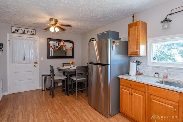 kitchen featuring brown cabinetry, freestanding refrigerator, decorative backsplash, light wood-style floors, and a textured ceiling