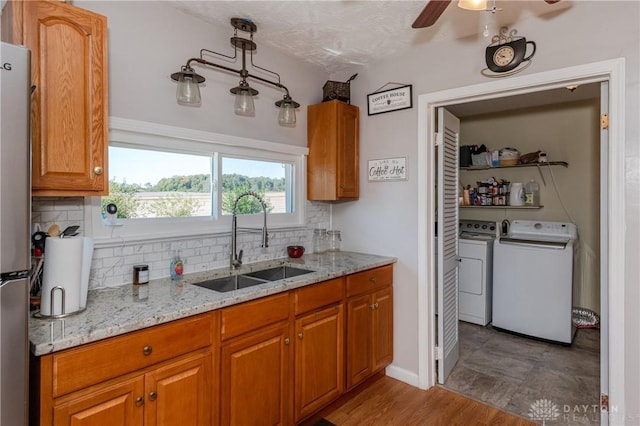 kitchen featuring light stone countertops, decorative backsplash, brown cabinetry, washer and dryer, and a sink