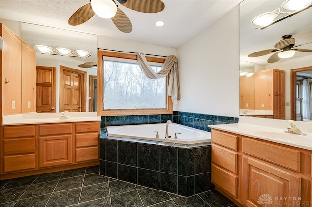 bathroom featuring tile patterned flooring, a relaxing tiled tub, ceiling fan, and vanity