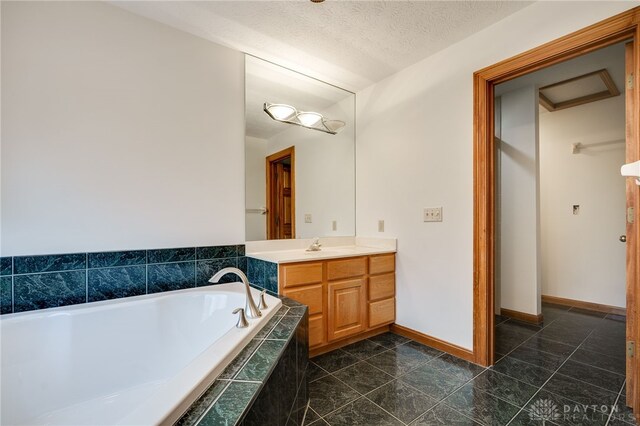 bathroom with vanity, tiled tub, and a textured ceiling