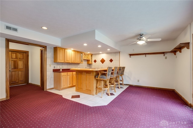 kitchen with light brown cabinets, ceiling fan, tasteful backsplash, light tile patterned floors, and a breakfast bar