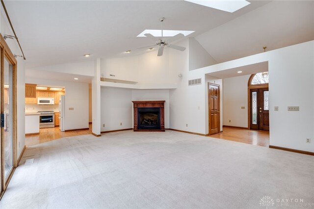 unfurnished living room featuring high vaulted ceiling, light colored carpet, a skylight, and ceiling fan