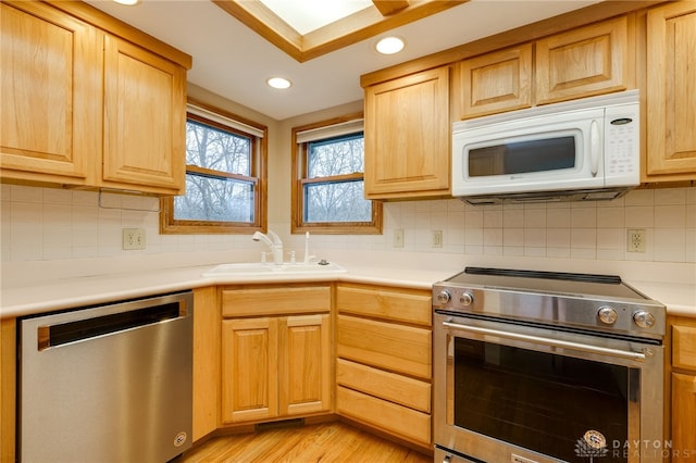 kitchen with sink, tasteful backsplash, light hardwood / wood-style flooring, and appliances with stainless steel finishes