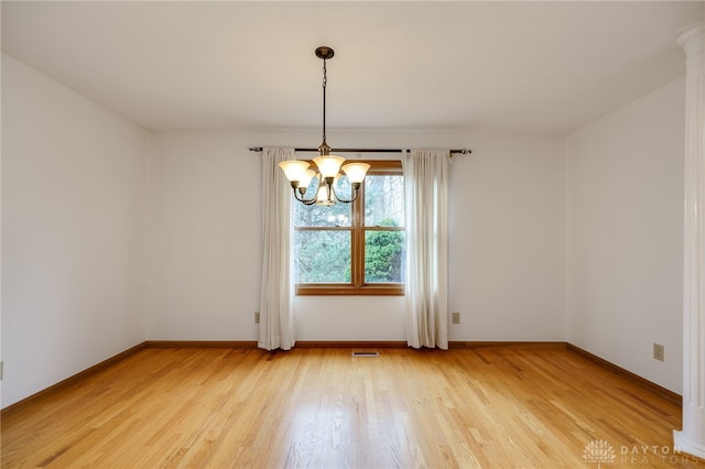 unfurnished dining area featuring a notable chandelier, hardwood / wood-style floors, and ornate columns