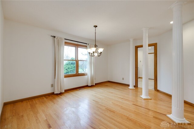 unfurnished dining area featuring light wood-type flooring, a notable chandelier, and ornate columns