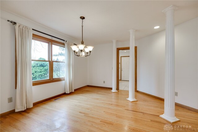 unfurnished dining area with a notable chandelier, ornate columns, and wood-type flooring