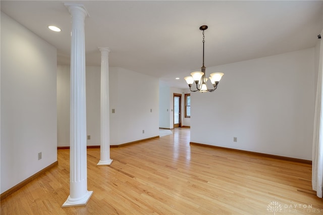 empty room with decorative columns, light hardwood / wood-style floors, and an inviting chandelier