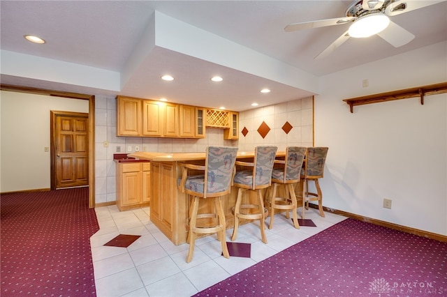 kitchen with light brown cabinetry, kitchen peninsula, backsplash, a breakfast bar area, and light tile patterned flooring