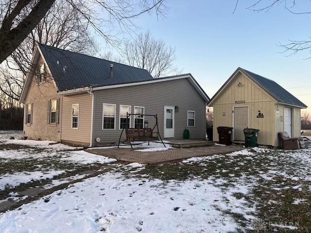 snow covered back of property featuring an outdoor structure