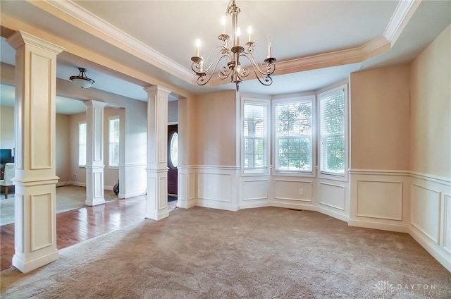 carpeted spare room featuring decorative columns, an inviting chandelier, and crown molding