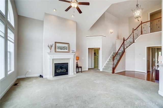 unfurnished living room featuring ceiling fan with notable chandelier, carpet floors, and high vaulted ceiling