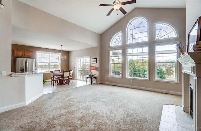 carpeted living room with ceiling fan with notable chandelier, vaulted ceiling, and a tiled fireplace