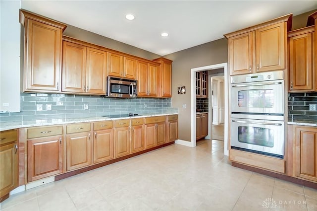 kitchen with light stone countertops, black electric cooktop, multiple ovens, and tasteful backsplash