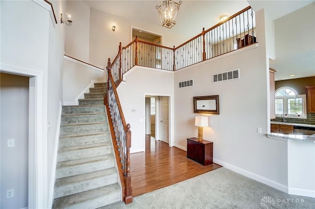 stairs with carpet, a high ceiling, an inviting chandelier, and sink