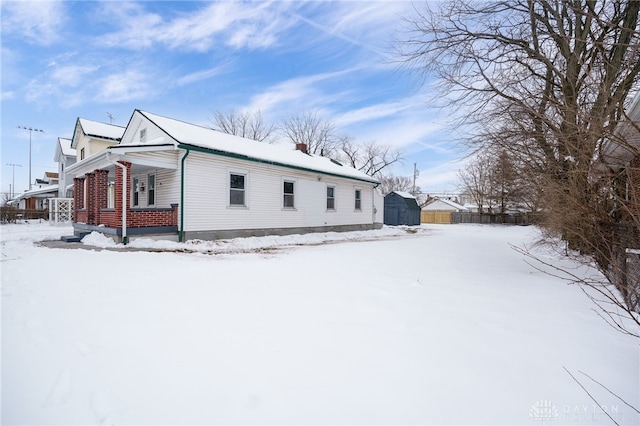 view of snow covered exterior with a storage shed and a porch