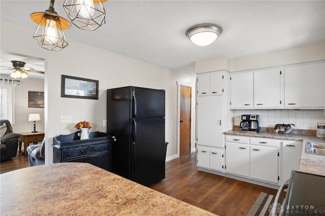 kitchen featuring dark wood-type flooring, white cabinets, black refrigerator, decorative backsplash, and decorative light fixtures