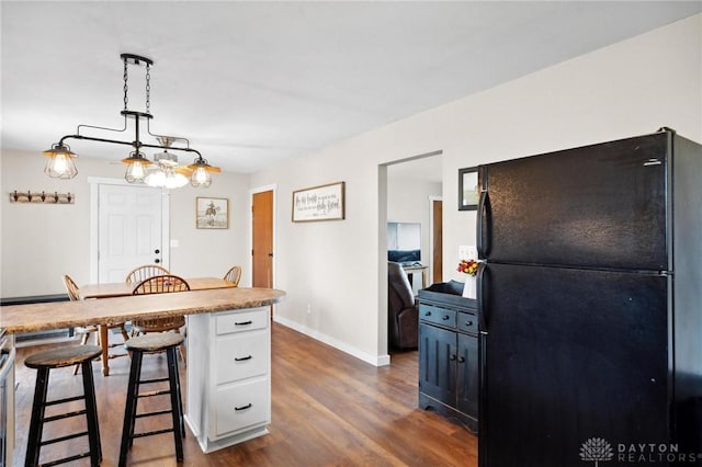 kitchen with pendant lighting, black refrigerator, dark hardwood / wood-style flooring, white cabinetry, and a breakfast bar area