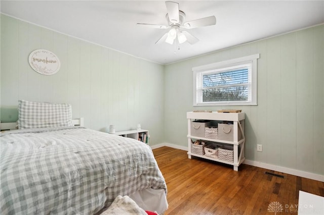 bedroom with ceiling fan, wooden walls, and hardwood / wood-style flooring