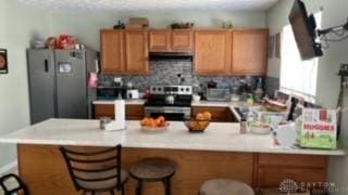 kitchen with kitchen peninsula, ventilation hood, stainless steel appliances, and tasteful backsplash