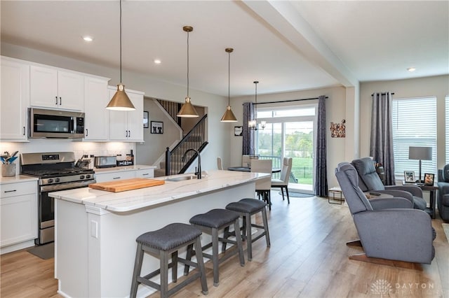 kitchen with a center island with sink, white cabinets, sink, appliances with stainless steel finishes, and decorative light fixtures