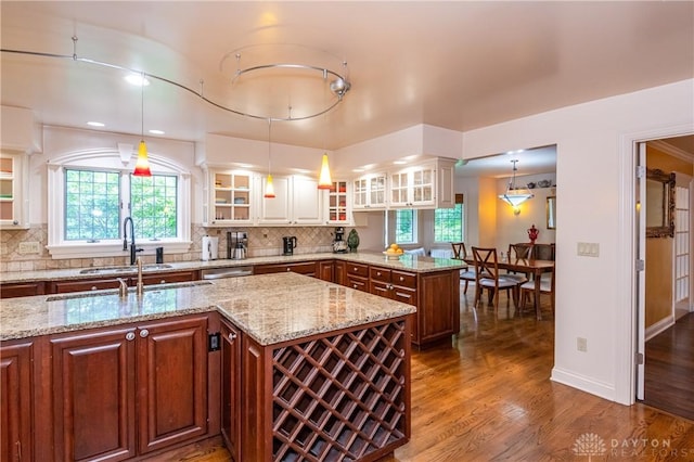 kitchen featuring light stone countertops, decorative backsplash, sink, decorative light fixtures, and a center island