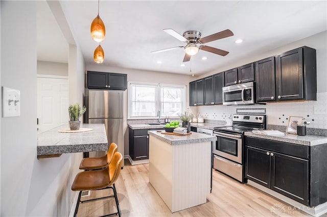 kitchen featuring sink, appliances with stainless steel finishes, decorative light fixtures, a kitchen island, and a breakfast bar area