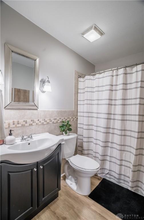 bathroom featuring hardwood / wood-style floors, toilet, vanity, tile walls, and a shower with shower curtain