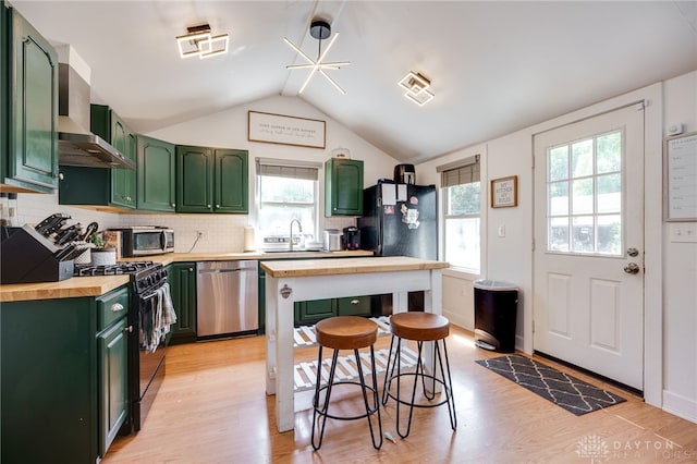 kitchen with butcher block counters, wall chimney exhaust hood, stainless steel dishwasher, black range with gas cooktop, and vaulted ceiling