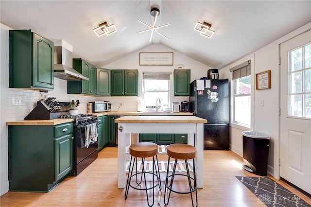 kitchen with lofted ceiling, black appliances, wall chimney exhaust hood, butcher block countertops, and plenty of natural light